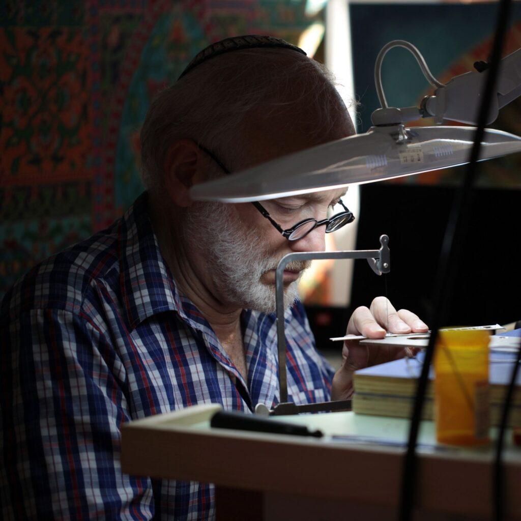 Ely Greenhut at his jeweler's bench under a magnifying lamp, sawing a pendant